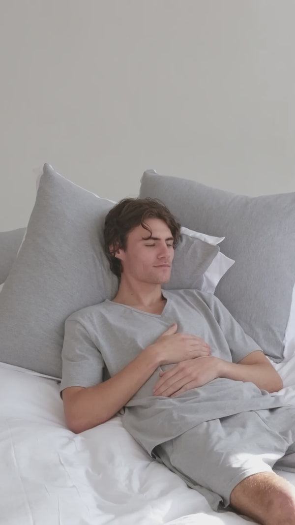 Model lounging in The T‑Shirt Bed Co. soft grey loungewear set beside Scandinavian White bedding, soft cotton, non‑iron luxury